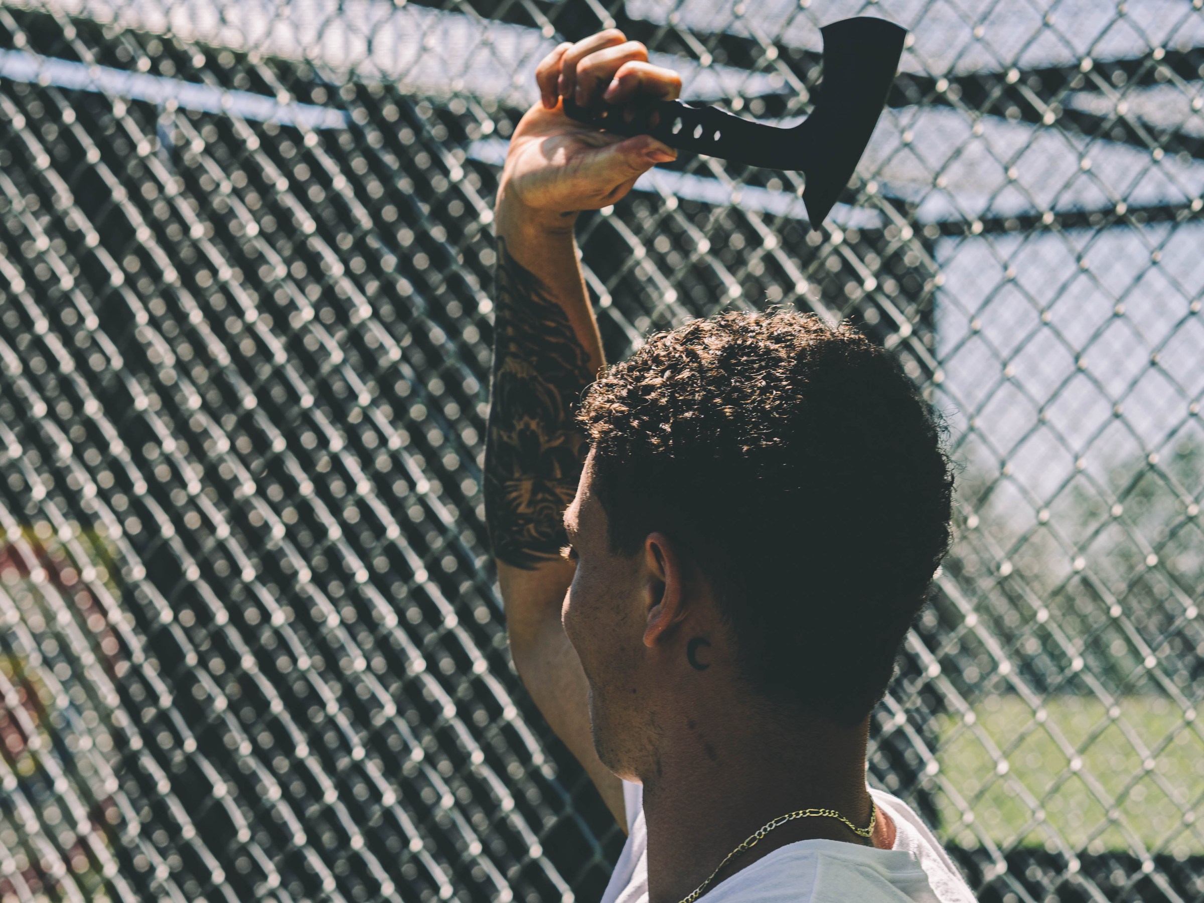 Person holding an axe near a chain-link fence outdoors.