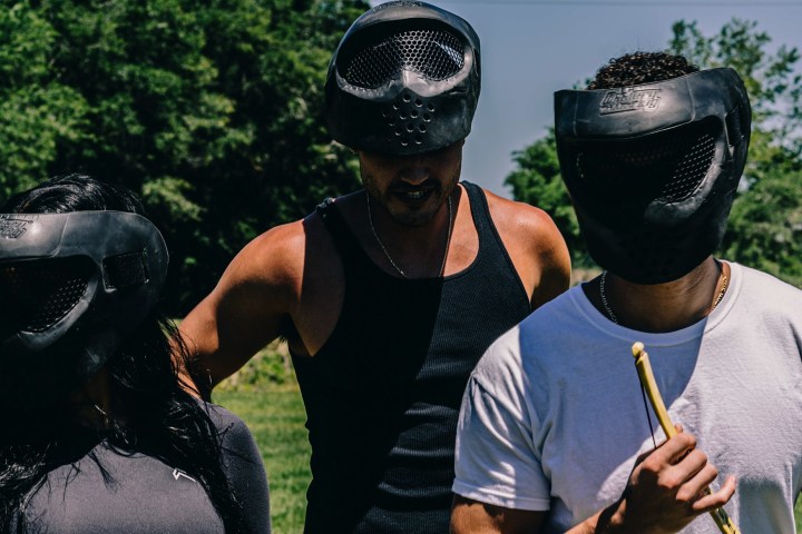 Three people wearing black paintball masks outdoors.