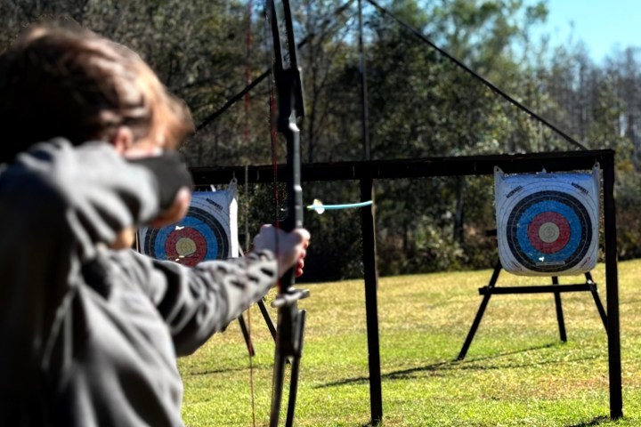 Person aiming bow at archery targets in grassy field.
