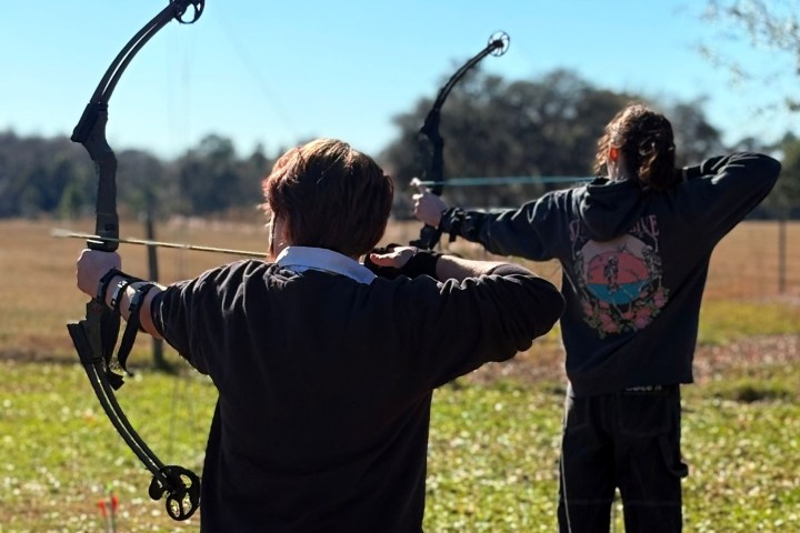 Two people practicing archery outdoors with compound bows.