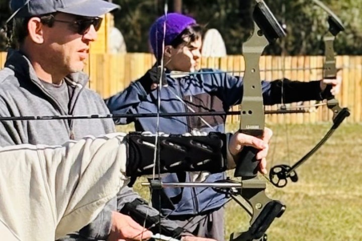 Two people practicing archery outdoors with compound bows.