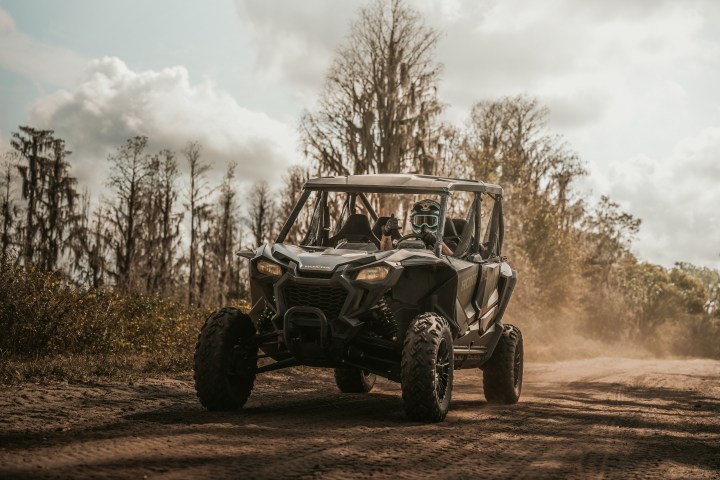 An ATV driving on a dirt path through a wooded area on a cloudy day.