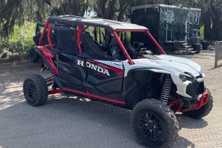 Red and white off-road vehicle parked on dirt under trees.
