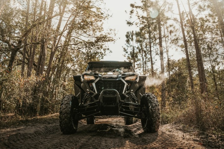 ATV on a dirt path in a forest with trees and sunlight filtering through.
