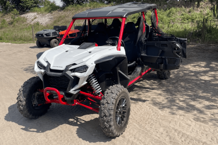 Off-road vehicle with red frame and black roof on sandy terrain.
