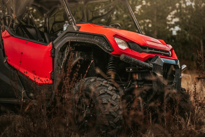 Red all-terrain vehicle parked on grassy field, forest background.