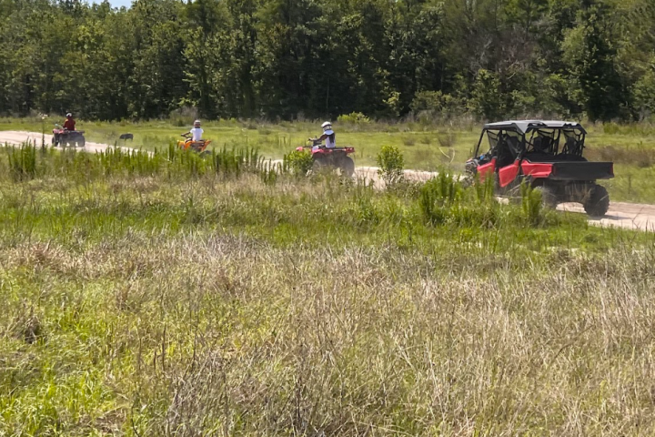 People riding ATVs and a side-by-side on a grassy trail.