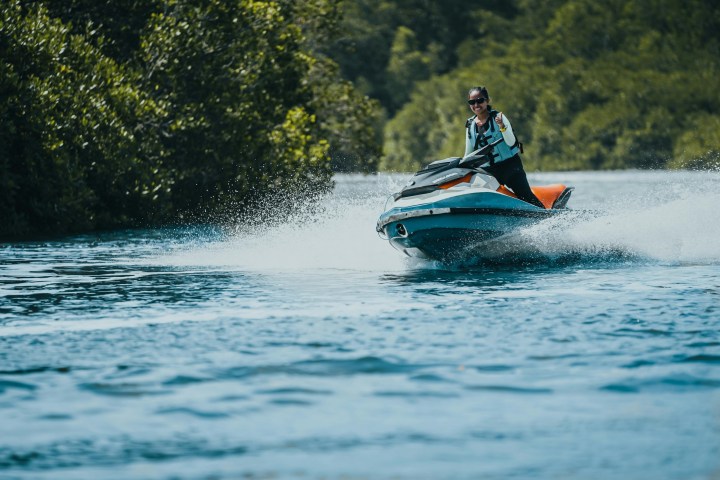 Person riding a jet ski on a river with lush green trees in the background.