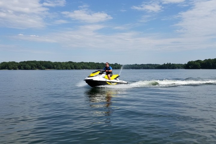Person riding a yellow jet ski on a calm lake under a blue sky.
