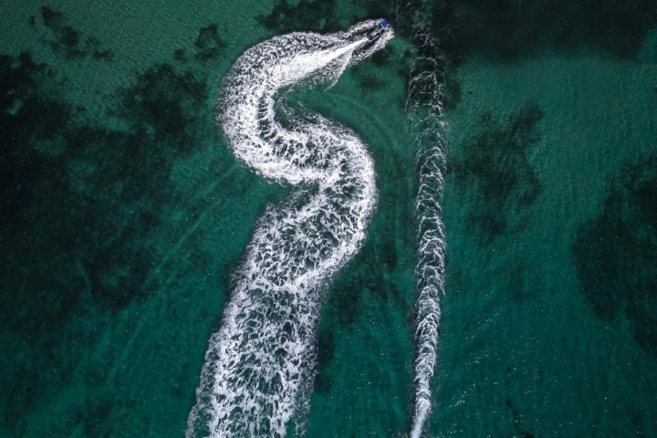 Aerial view of two boats creating white trails on turquoise water.