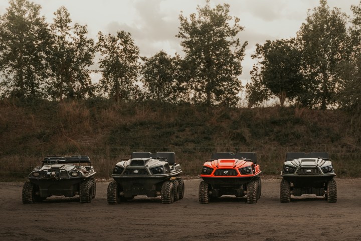 Four all-terrain vehicles parked on a dirt road with trees in the background.