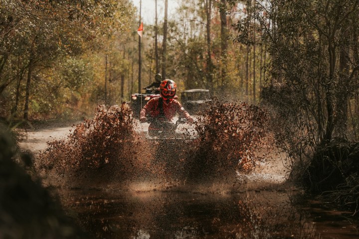 Person on ATV splashing through muddy water in a forest.
