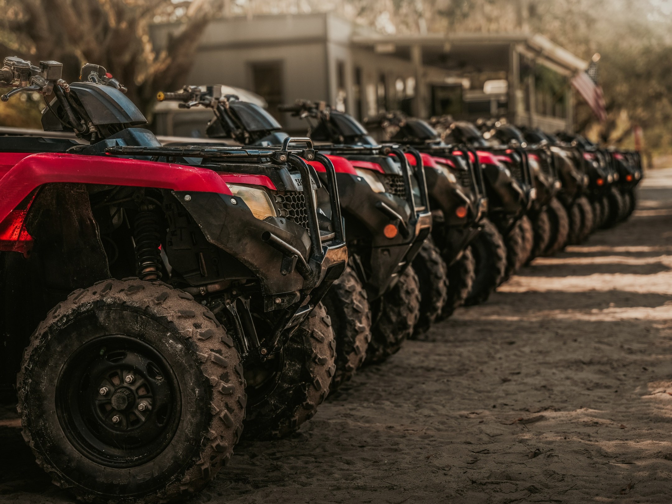 Line of red and black ATVs parked on a dirt path outdoors.