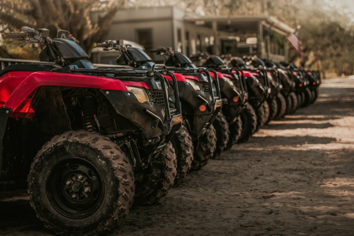 Line of red and black ATVs parked on a dirt path outdoors.
