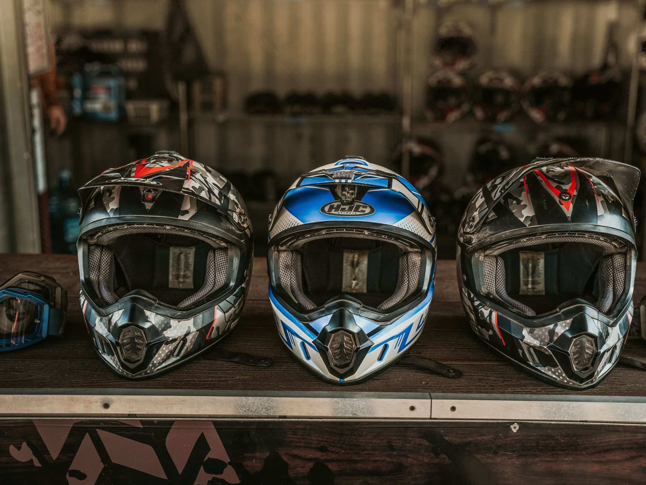 Three motocross helmets on display with goggles beside them.