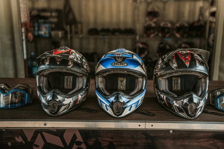 Three motocross helmets on display with goggles beside them.