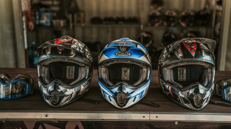 Three motocross helmets on display with goggles beside them.