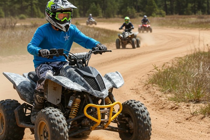 People riding ATVs on a dirt track, wearing helmets and protective gear.